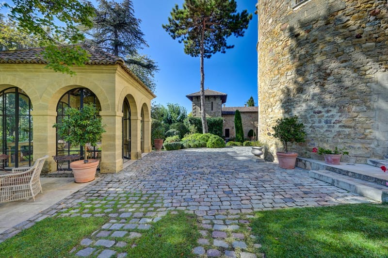 Chateau courtyard with stone orangery, medieval tower, cobblestones, and topiary gardens