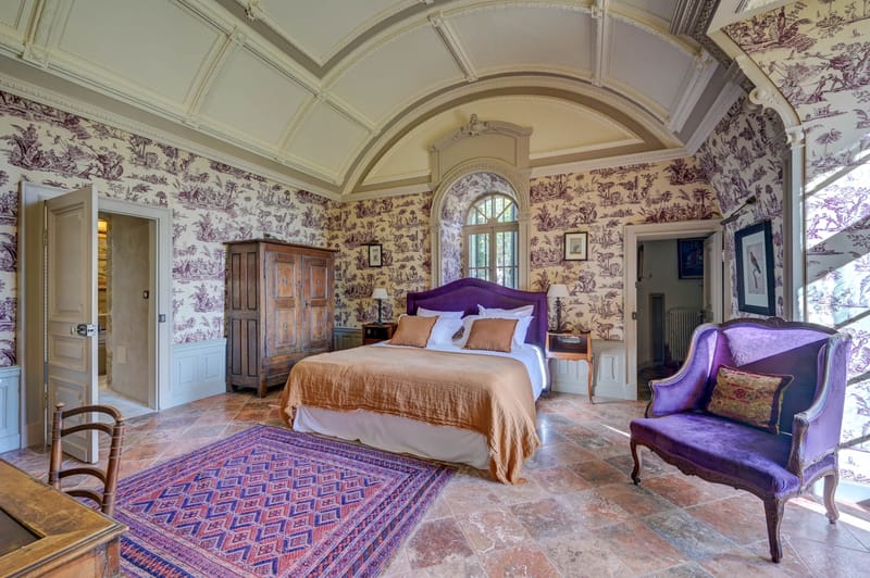 Chateau bridal suite with barrel-vaulted ceiling, purple toile wallpaper, antique armoire and velvet armchair