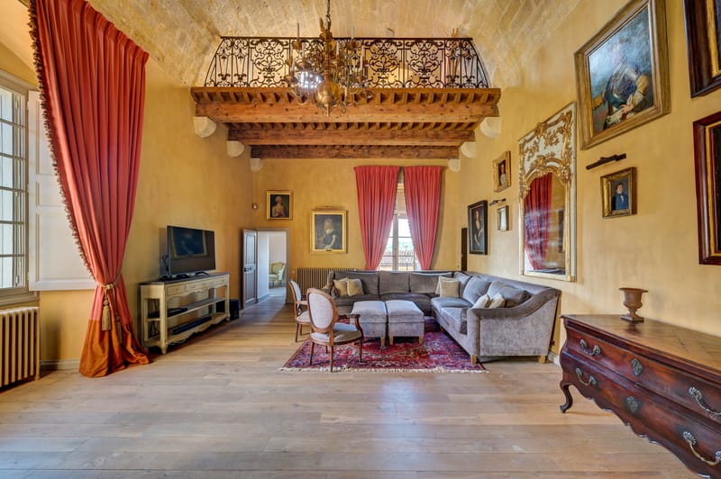 Grand chateau salon with vaulted beamed ceiling, wrought-iron mezzanine, paintings, and antique furnishings