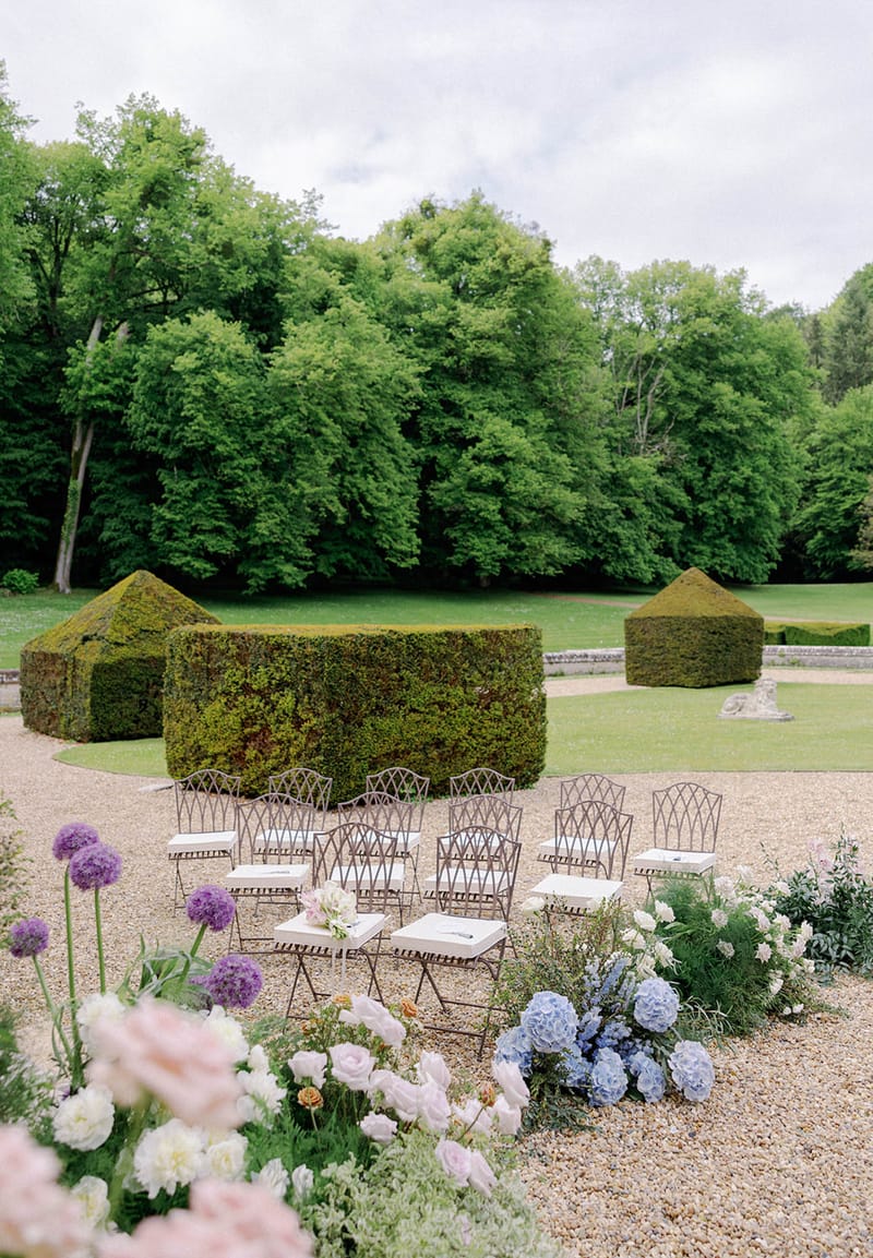 Outdoor ceremony setup with wrought-iron chairs in formal garden courtyard with topiary backdrop
