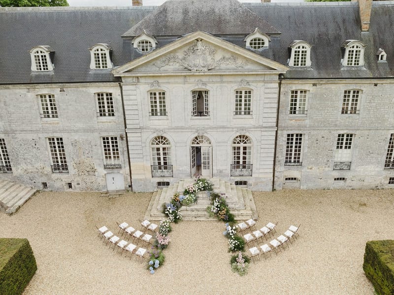 Aerial view of wedding ceremony setup in château courtyard with white chairs and floral arrangements