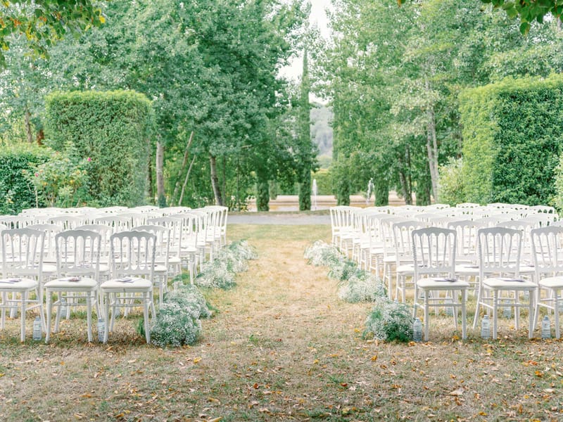 White Napoleon chairs with gypsophila aisle markers in formal hedged garden allee before ceremony