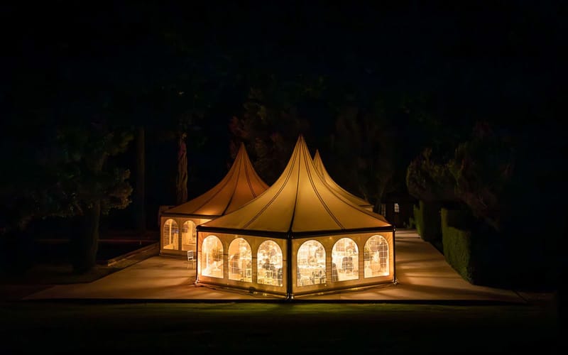 Night view of glowing pagoda marquee tent with guests visible through clear panels at chateau grounds