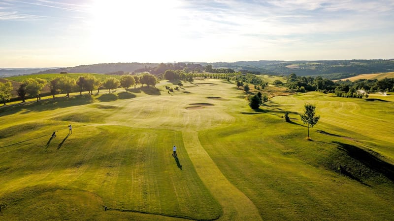 Aerial view of golf course fairways with sand bunkers and chateau visible among distant trees