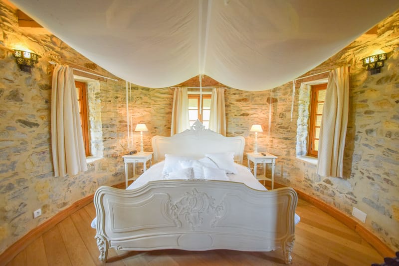 White-canopied Louis XV bed in stone-walled chateau bridal suite with Moorish sconces and oak floor