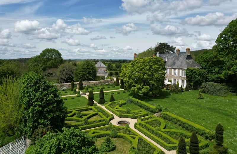 Aerial view of Norman stone manor with formal French parterre garden, clipped box hedges, and open countryside