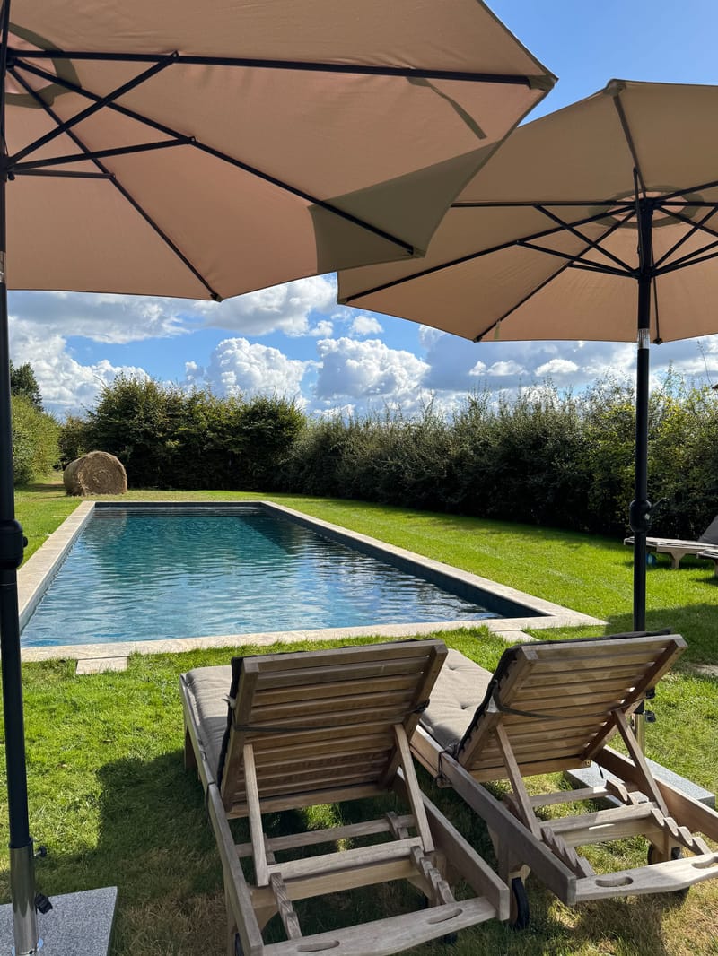 Swimming pool area with wooden sun loungers and parasols on lawn at French manor venue on a sunny day