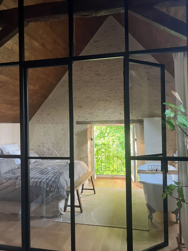 Venue bedroom suite with exposed stone walls, clawfoot bathtub, and wooden beams seen through crittall glass partition