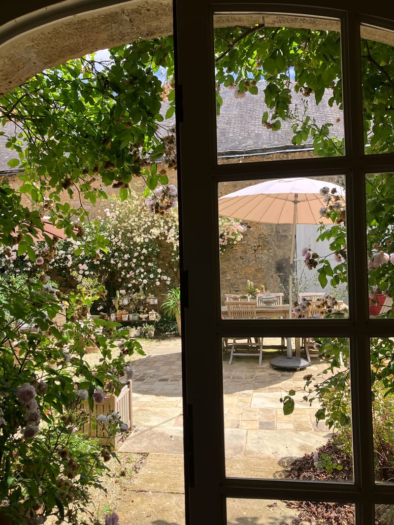 Walled courtyard garden with climbing blush roses framing stone archway and shaded dining table