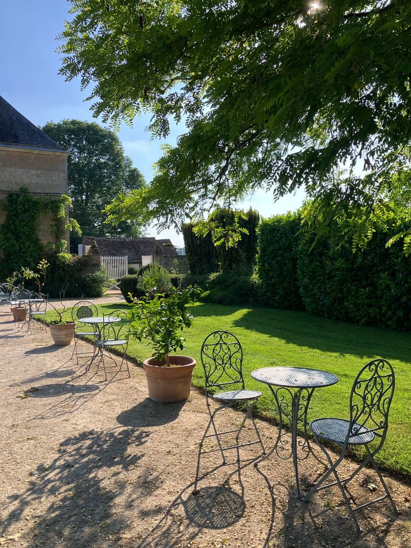 Gravel terrace with wrought-iron bistro seating and terracotta pots beside a stone chateau facade