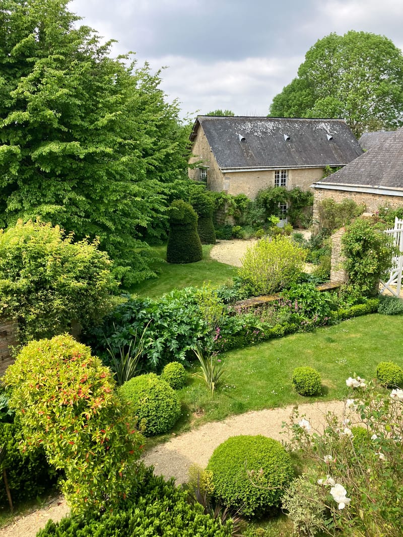 French stone manor house garden with clipped topiaries, gravel paths, white roses, and wooden bench