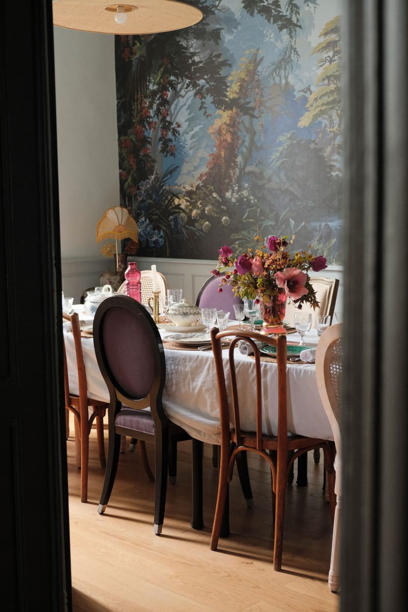 Eclectic dining room with panoramic woodland mural, magenta poppies, velvet chairs, and cane-back seating