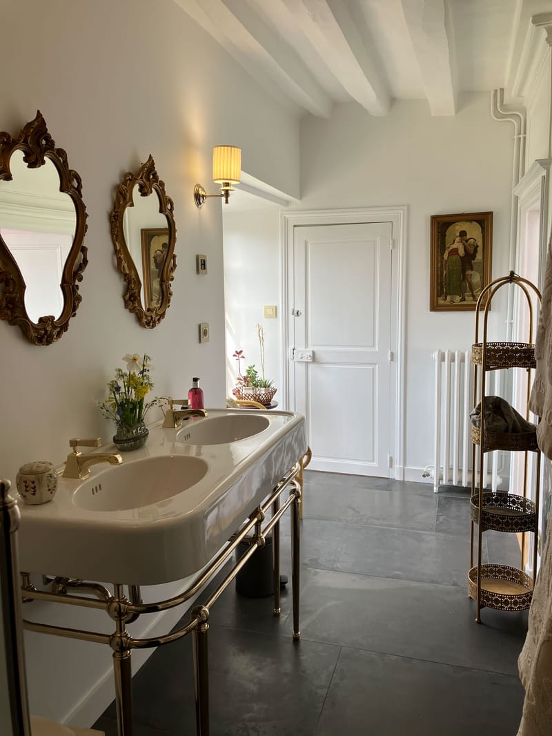 Venue bathroom with double basin on brass frame, baroque gilt mirrors, and exposed white ceiling beams