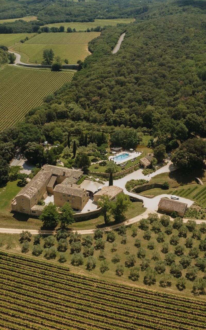 Aerial view of golden stone Provencal mas estate with pool, vineyards, and olive grove surroundings