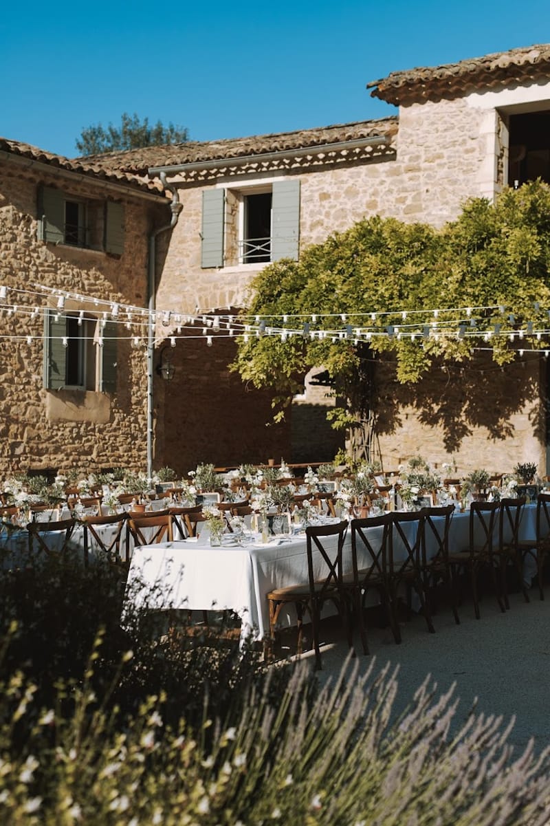 Courtyard reception at stone Provencal mas with banquet tables, cross-back chairs, and string lights overhead