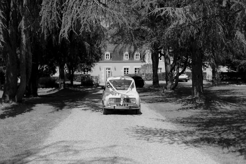 Vintage Renault 4CV wedding car on gravel driveway approaching French manor house with tree-lined entrance