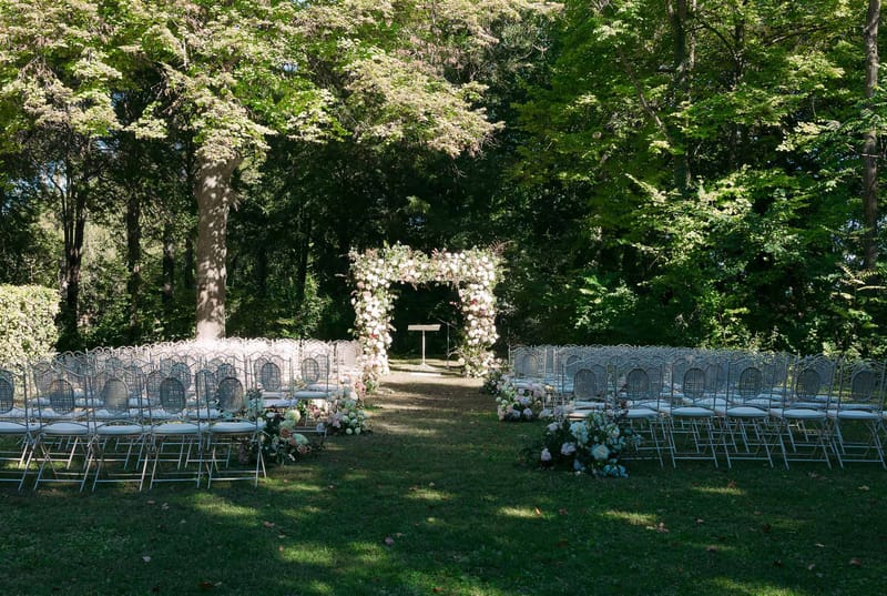 Outdoor wedding ceremony setup with floral arch in wooded garden venue