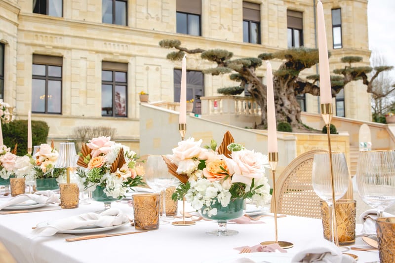 Reception table with blush roses in teal bowls, gold candleholders, and dried palm leaves at chateau