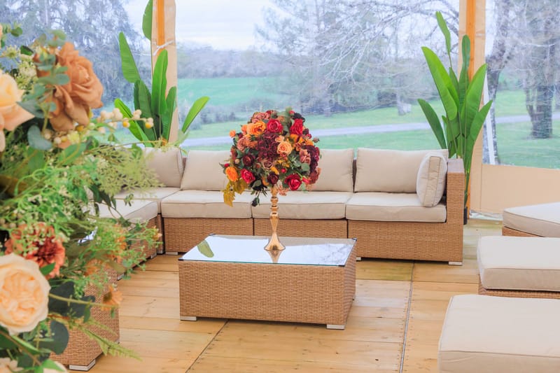 Marquee lounge area with wicker sofa and autumn floral arrangements in burgundy, orange, and peach tones