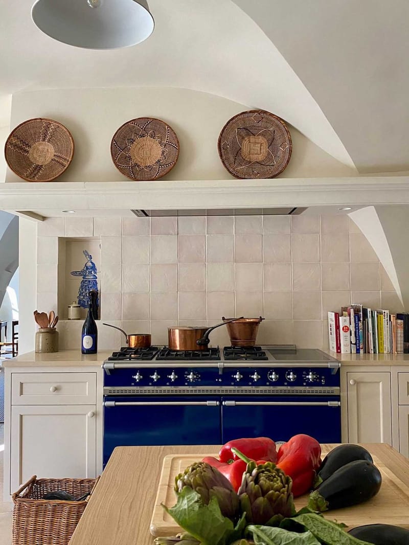 Kitchen interior with cobalt blue range cooker, copper pots, zellige tile backsplash, and fresh vegetables