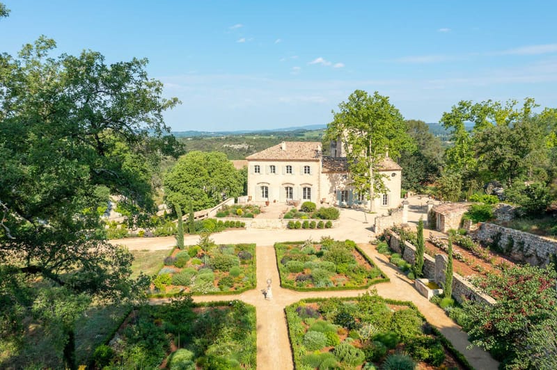 Aerial view of Provencal stone manor with terracotta roof, parterre garden, and valley landscape beyond