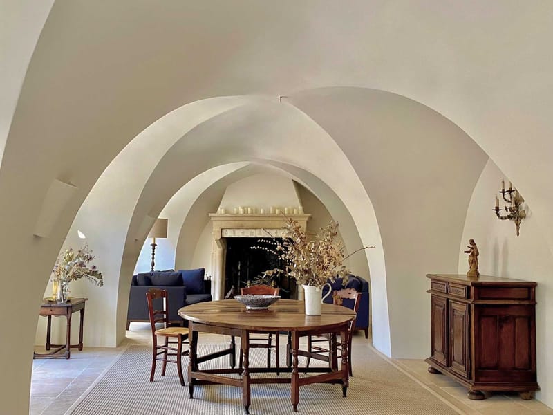 Barrel-vaulted white plastered interior with walnut table rush chairs fireplace and dried flowers