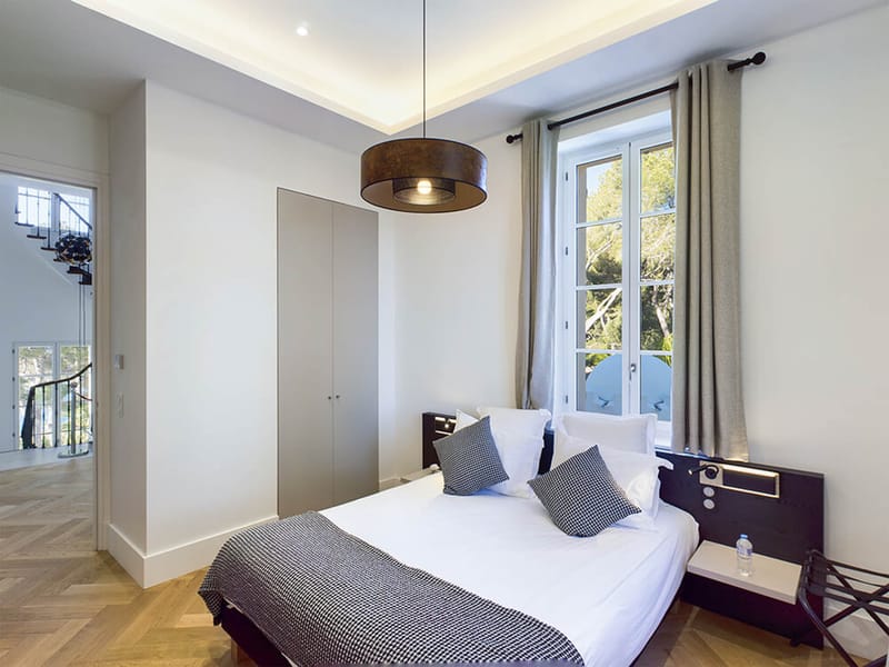 Guest bedroom with white linens and herringbone parquet flooring at French venue with wrought iron staircase