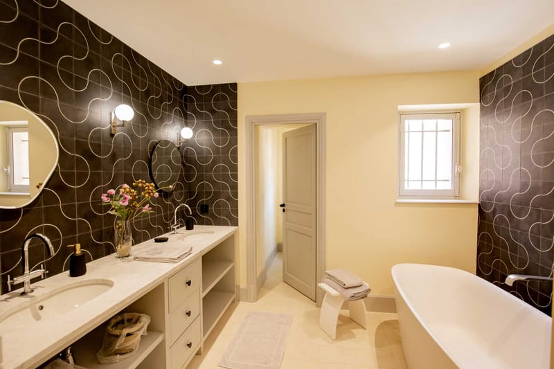Bridal suite bathroom with freestanding bathtub, double vanity, charcoal accent tiles, and globe sconces
