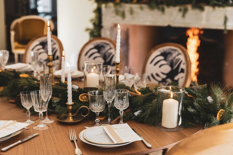 Pine garland runner with dried oranges, brass candlesticks, and gold-rimmed chargers beside lit fireplace