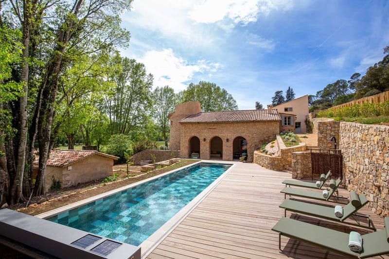 Provencal stone mas with arched pool house, turquoise lap pool, wood deck, and olive-green sun loungers