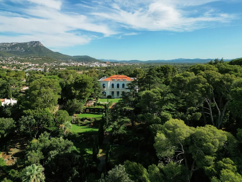 Aerial view of Belle Epoque villa surrounded by trees with mountain backdrop at Domaine Rocabella, French Riviera