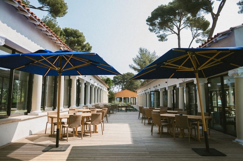 Courtyard dining terrace with blue parasols and pine trees at Domaine Rocabella, French Riviera