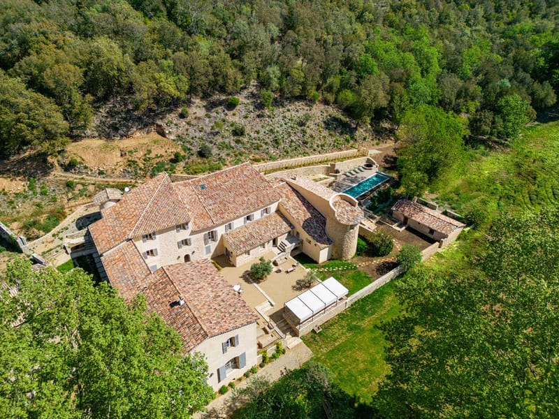 Aerial view of stone bastide with terracotta roofs, round tower, courtyard, pool, and white marquee tent