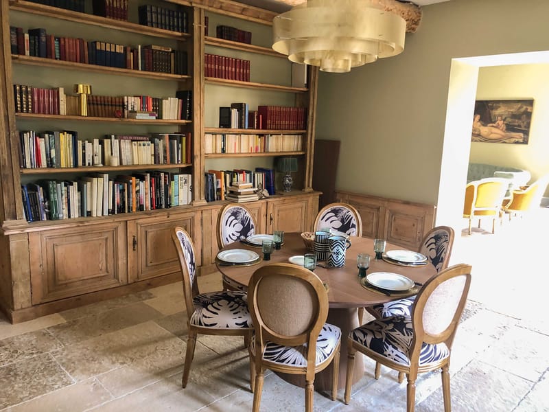 French country dining room with round table, tropical print chairs, and floor-to-ceiling bookcase