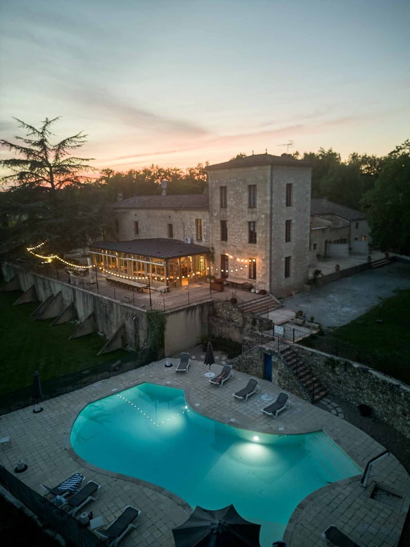Dusk aerial of illuminated pool and chateau with string lights at Chateau de Sanse