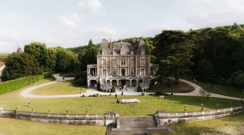 Aerial view of 19th-century brick and stone chateau with curved staircase and lawn table setup