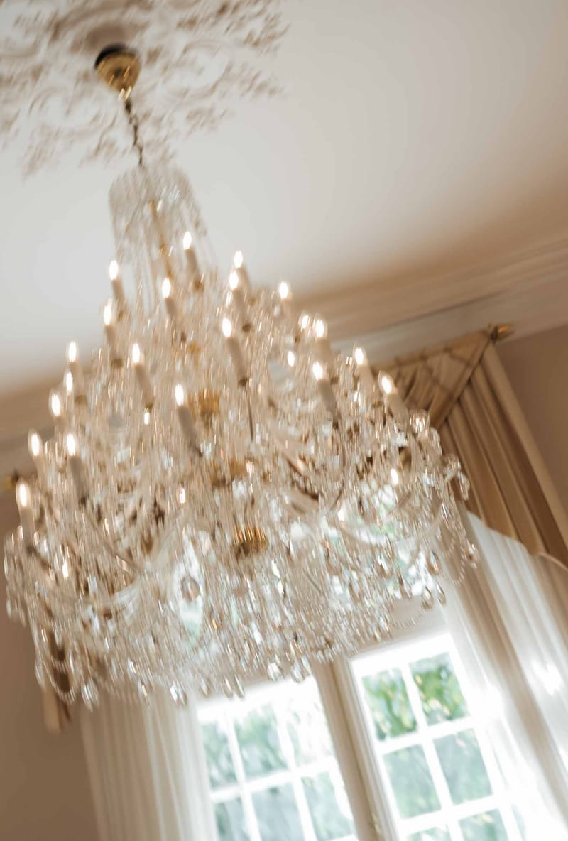 Multi-tiered crystal chandelier with gold fitting beneath ornate plaster ceiling with champagne drapes