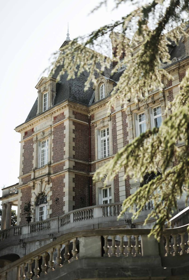 Red brick French chateau corner facade with cream stone detailing and slate mansard roof framed by blossoming branches