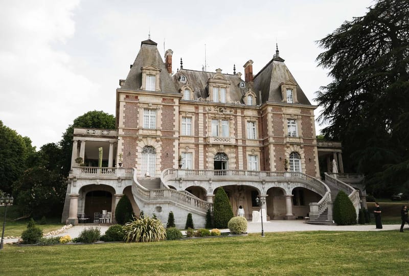 Grand red brick and limestone chateau with mansard roof, sweeping double staircase, and manicured topiary gardens