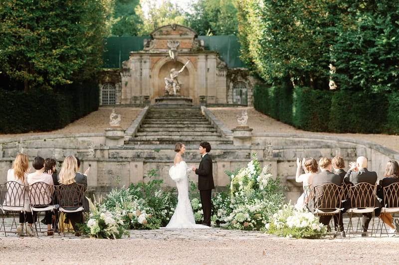 Vow exchange before stone staircase with white hydrangea ground installation in formal garden