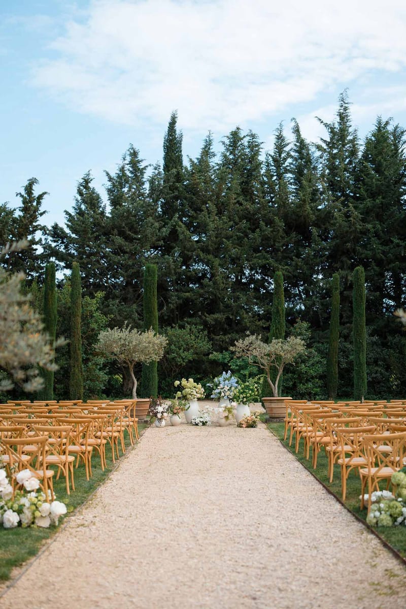Outdoor wedding ceremony setup with wooden chairs and floral arrangements in Mediterranean garden setting