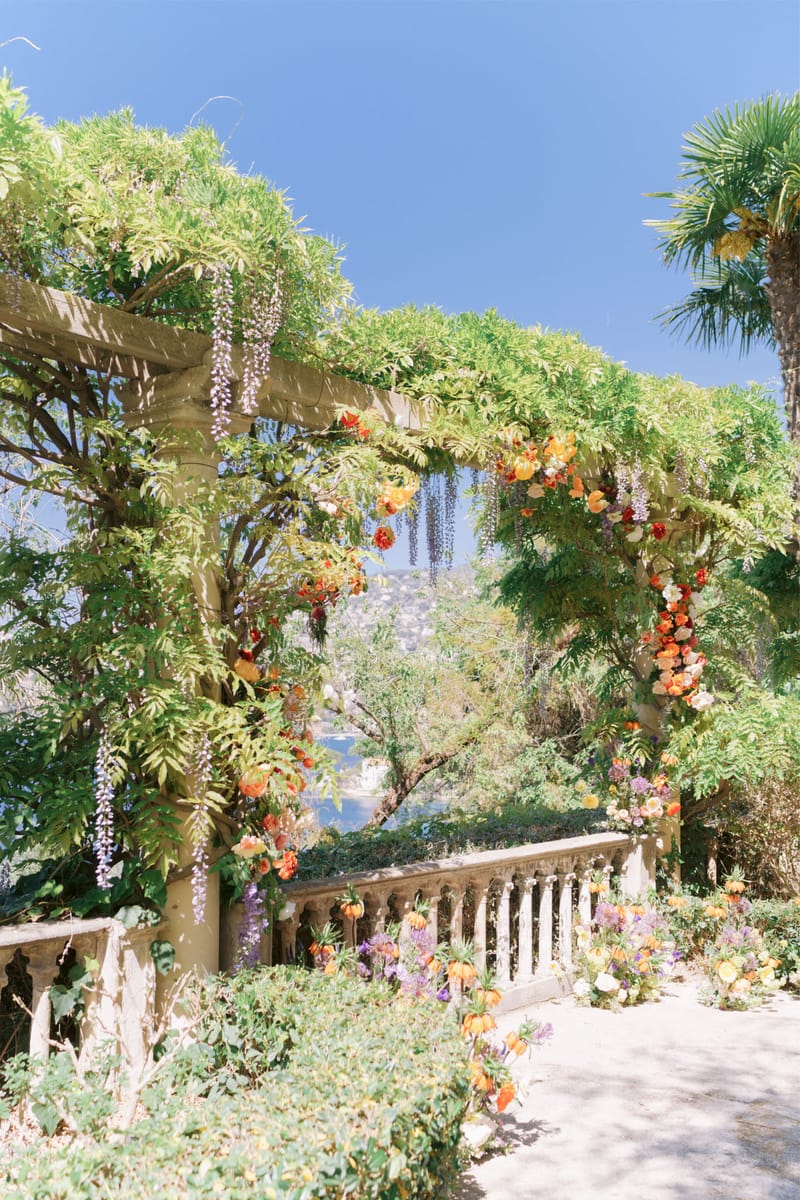 Stone pergola draped with wisteria and decorated with orange ranunculus and crown imperial lilies on a villa terrace