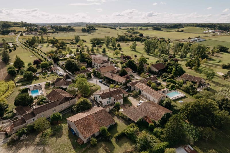 Aerial view of stone estate with two pools, marquee tent, and surrounding countryside and vineyards