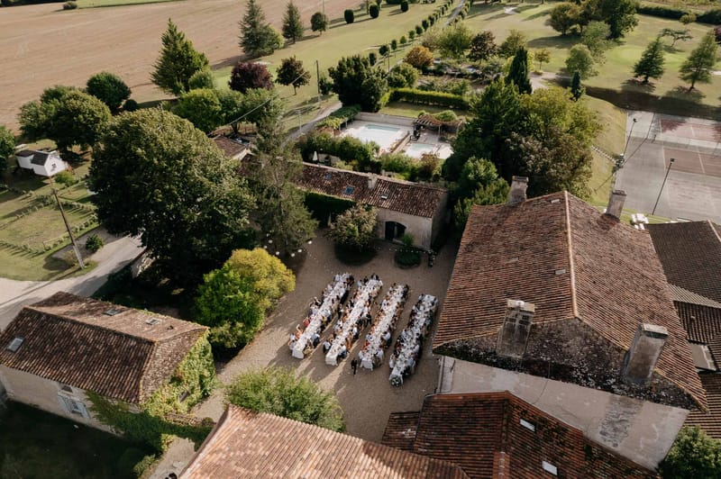 Aerial view of 100-guest dinner in estate courtyard with pool, tennis court, and tree-lined avenue