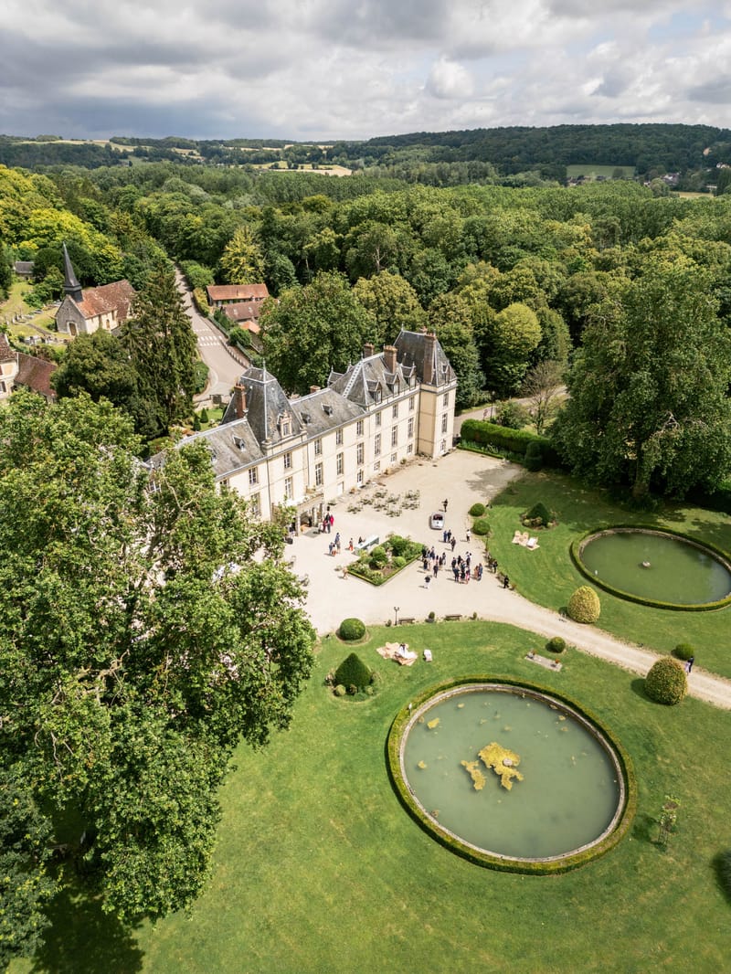 Aerial Renaissance chateau with mansard roof towers formal gardens ornamental ponds and stone church in woodland