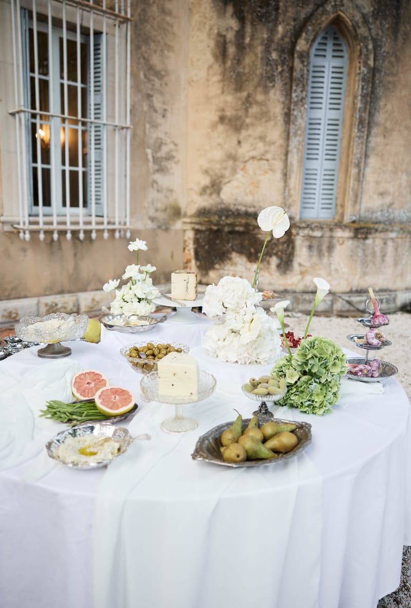Grazing table with white hydrangeas calla lilies cheeses and fruits before chateau stone facade
