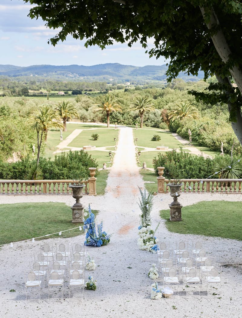 Elevated view of an outdoor ceremony setup with blue and white florals and acrylic chairs on a chateau terrace