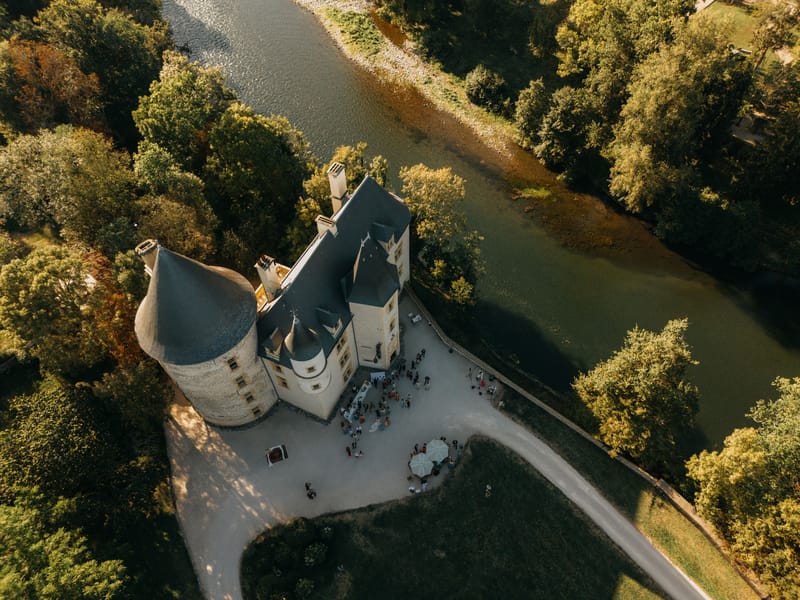 Aerial drone view of wedding cocktail hour at a French chateau on a river peninsula with guests on gravel courtyard