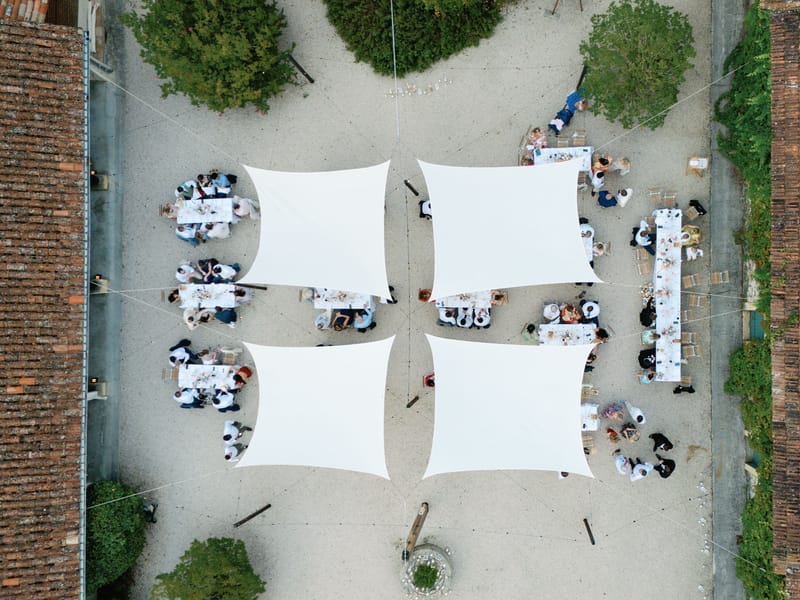 Aerial view of outdoor wedding reception under white sail canopies in a chateau courtyard with long dining tables