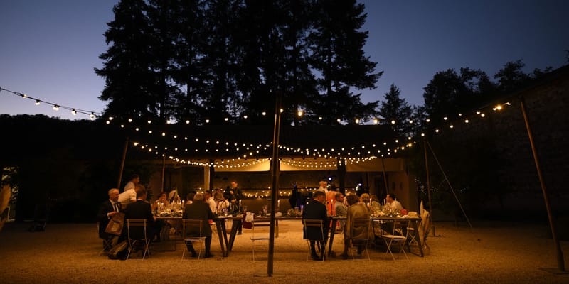 Dusk courtyard reception with festoon lights long banquet tables and stone building backdrop